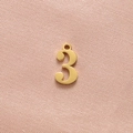 Detail of a matte gold-finished number 3 pendant with a hanging loop on fabric - Gold Number 3