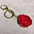 Detalle de llavero con rodaja de ágata roja y borde dorado sobre un fondo gris - Tamaño Irregular / Rojo Brillante