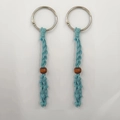 Dettaglio del portachiavi a rete intrecciato azzurro con perla in legno marrone e anello metallico - Azzurro