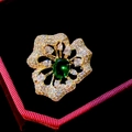 Close-up of a flower-shaped gold brooch with clear diamonds and a large emerald centerpiece - Green Round Gem Floral Style (B888)