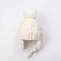 Detail of white winter knit hat featuring a fluffy pom-pom and protective earflaps - S / Milk White