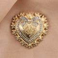 Dettaglio macro di una spilla a cuore dorata con strass e fiocco su seta beige - Cuore Oro con Fiocco (XD10525)