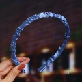 Detail of blue pleated satin headband with glossy texture held by hand for display - Blue (Satin Pleated)