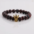 Detail of dark red faceted bead bracelet featuring a metallic golden crown charm - Red Tiger Eye