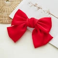 Close-up of a large red satin bow hair clip on a white magazine with cotton branch decor - Spring Clips / Red