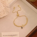 Dettaglio del bracciale a catena dorata con lettera H in pavé e ciondolo malocchio - Lettera H