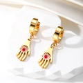 Macro shot of gold Hamsa hand earrings with Evil Eye inlay on white marble stand - Red Eye Hamsa