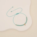 Macro shot of turquoise braided bracelet with faceted beads and a crystal heart pendant - Solid Green