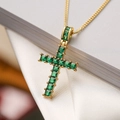 Macro view of gold cross necklace with emerald green square-cut gemstones - Green