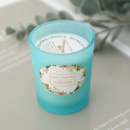 Blue frosted glass scented candle with white soy wax and floral label in a serene setting - Lime Basil & Mandarin
