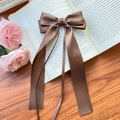 Elegant brown satin ribbon bow hair clip displayed on an open vintage book page - Medium Coffee