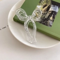 Close-up of a transparent jelly bow hair claw clip placed on a decorative white plate - Clear White