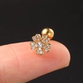 Macro detail of a golden flower cartilage stud with clear crystals on a fingertip - CC027-2 Gold Four Leaf Clover