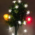 Close-up of snowflake LED string lights with cold white glow on green branches - Transparent Flat Snowflake / 1m 10-LED (2AA Battery Model)