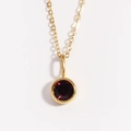 Detail of a gold birthstone necklace featuring a round red crystal pendant on a thin chain - June Alexandrite Purple