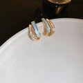 Macro shot of gold C-shaped earrings with light blue enamel and sparkling zircon accents - Blue Silver Needle Style