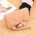 Beige long wallet with floral embossing, zip closure and wrist strap in hand - Camel