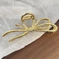Detailaufnahme der eleganten goldenen Haarklammer mit Schleife auf weißem Papierhintergrund - Gold