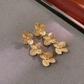 Dettaglio macro di orecchini pendenti a tre fiori dorati con finitura in ottone vintage - Orecchini / Oro