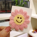 Pink knitted daisy hair clip with a cheerful brown smiley face on a yellow center - Pink Smiley Flower