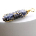 Blue spot stone hexagonal pendant with gold wire wrap on a minimalist display - Sodalite