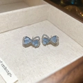 Gros plan de boucles d'oreilles nœud en argent avec pierre de lune bleue et zircons - Clous d'oreilles noeud saphir incrusté de strass (46# Tige en argent - Bleu) / Boucles D'oreilles Puces En Forme De Nœud En Métal Argenté Avec Une Pierre Principale Bleu Clair Semi-transparente Et Un Sertissage Entièrement En Diamants.