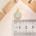Macro shot of a 1.3cm gold Evil Eye pendant with blue zircon stones on a scale ruler - E0012G