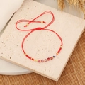 Detailed shot of handmade red cord bracelet with colorful glass beads on a textured surface - Red