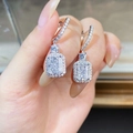 Orecchini pendenti in argento 925 con zircone a taglio radiant, tenuti a mano su sfondo sfocato - Bianco