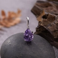 Macro shot of a purple teardrop gemstone pendant on silver base over a dark pebble - Natural Amethyst Water Drop Pendant Silver