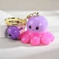 Close-up of pink octopus keychain with golden ring and purple bell on white stage - Bell Style [Purple]