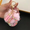 Detailed shot of pink pom-pom keychain with colorful heart sequins and golden clasp - Letter O