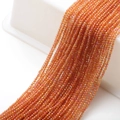 Close-up of orange faceted glass beads on cotton thread for DIY jewelry making - Gold Rose Red