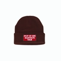 Macro shot of embroidered 'PUT IT ON SANTA'S TAB' red patch on a brown knit beanie - Coffee