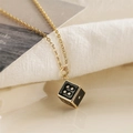 Collana dorata con ciondolo a forma di dado colorato su sfondo di tessuto beige - Nero