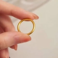 Close-up of a minimalist smooth golden titanium steel ring held between fingers - Size 5 / Gold