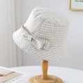Detail of a beige plaid bucket hat with a bow on a wooden stand in a soft sunlit setting - White Grid