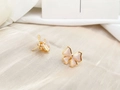 Detail view of gold-plated bow stud earrings with delicate pink enamel inlays - Cream