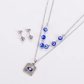 Detailed view of silver double-layered necklace and stud earrings with blue evil eye charms - Blue & Silver
