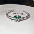 Macro-opname van zilveren vlinderarmband met sprankelende groene en witte zirkonia op porselein - Groen