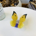 Detail of a translucent yellow acrylic butterfly hair claw with purple grip on a table - Approx 8.5cm / Yellow