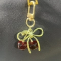 Close-up of a realistic red cherry pendant with golden bow on a metal keychain - Velvet Dark Red Cherry Gold Bow