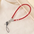 Close-up of a red rhinestone phone lanyard with metal clip on beige textured fabric - Red
