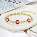 Dettaglio di un bracciale dorato con ciondoli a occhio turco rossi e pietre di zircone - Oro-Occhio del Diavolo Rosso