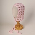 Detail of pink hand-knitted mohair baby bonnet with lace-up straps and hollow-out crochet pattern - Pink