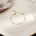 Detail van gouden armband met tandwielhangers op wit bord en paarse zijden achtergrond - Gouden Tandwiel(S225)