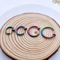 Macro shot of rainbow-colored stainless steel clip-on earrings in multiple sizes on wood - 2.0mm Wire Diameter 14mm Inner Diameter / Rainbow