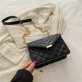 Elegant black quilted chain bag with gold hardware on a beige suit background - Black