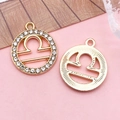 Golden Libra zodiac pendants with crystals and textured metal finish on pink background - Libra