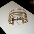 Detail eines mehrlagigen Gold-Armreifs mit Glitzereffekt und glatten Metallbändern - Gold